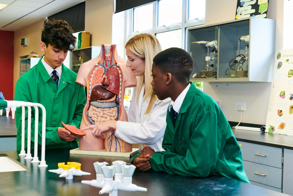 a picture of two students and a teacher looking at a model of the human body