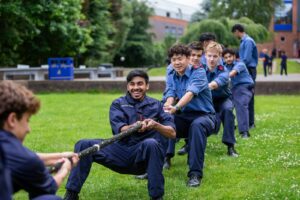 A group of six boys dressed in blue CCF navy uniform pulling on a rope during tug of war.