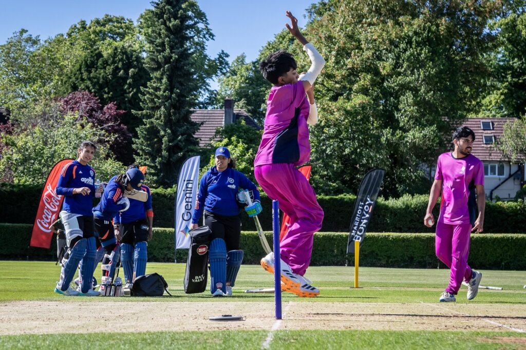 Student in purple net bowling kit in his bowling action, watched on by India players