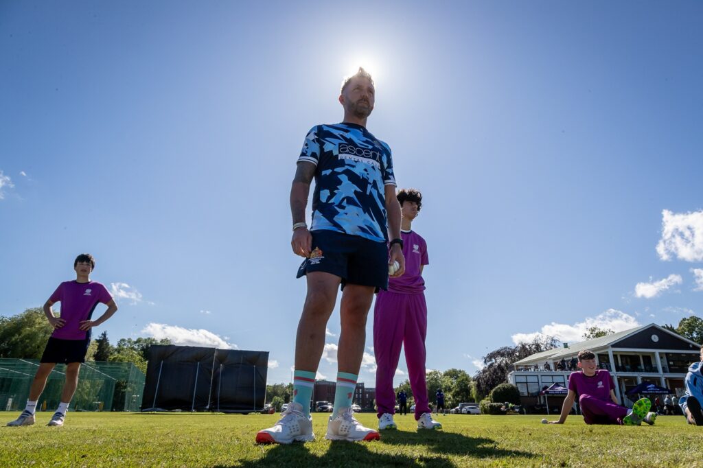 KES Director of Cricket standing with a student to his right, the sun shining brightly behind them