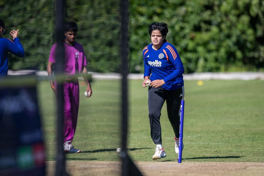 India player about to bowl, watched on by student player