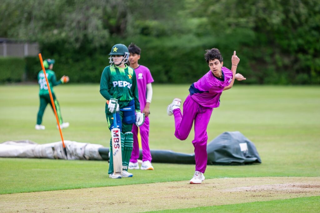 Student in purple net bowling kit bowling, with Pakistan player stood behind