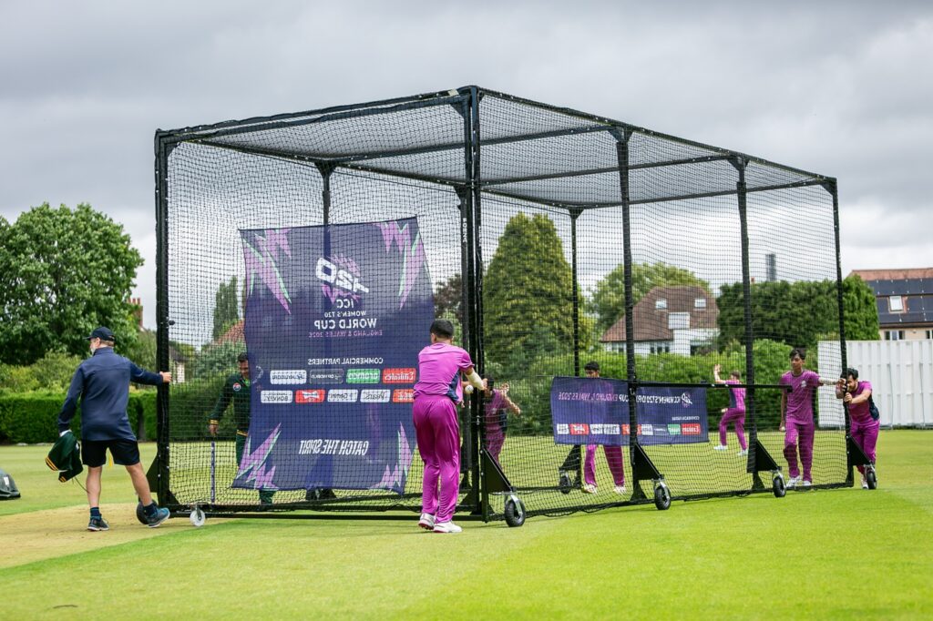 Students in purple net bowling kit moving some cricket nets