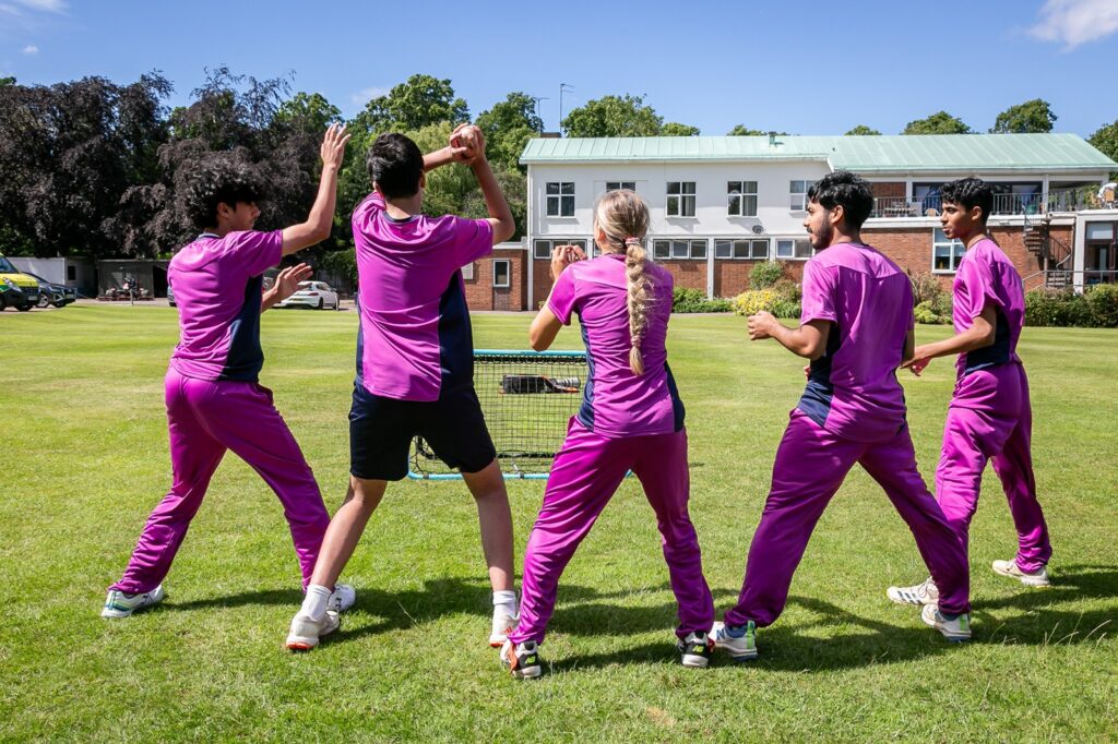 Looking towards the backs of student cricketers waiting to catch a cricket ball thrown at a net