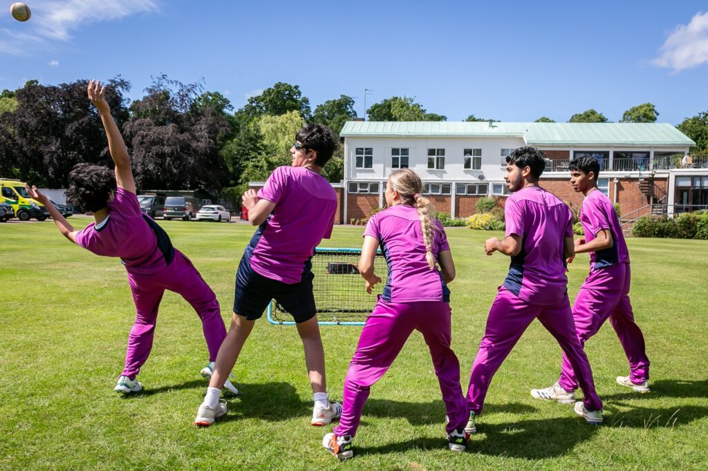 Student cricketers in a line, waiting to catch a ball thrown at a net which is just about to go past one of them