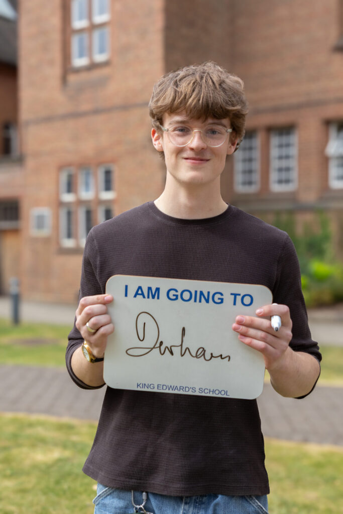 A boy holding a sign that says "I AM GOING TO Durham" and "KING EDWARD'S SCHOOL".