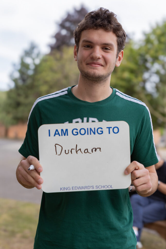 A boy holding a whiteboard that says "I AM GOING TO Durham" and "KING EDWARD'S SCHOOL".