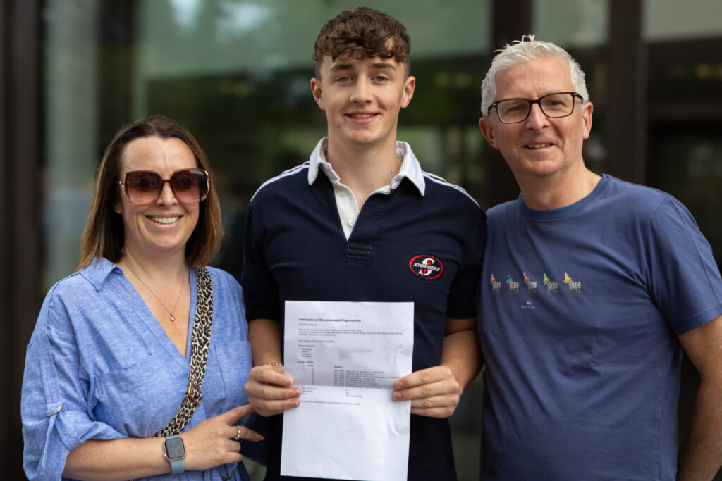 A boy stands between two adults, holding a document. They are all smiling and celebrating an achievement.