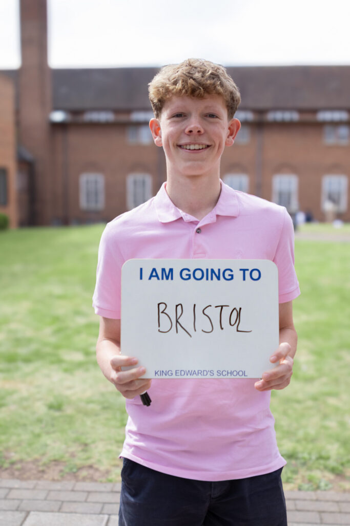 A boy holds a sign that says "I AM GOING TO BRISTOL KING EDWARD'S SCHOOL".