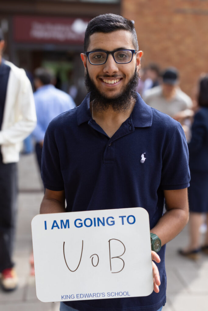 A boy holding a sign that says "I AM GOING TO UoB KING EDWARD'S SCHOOL".