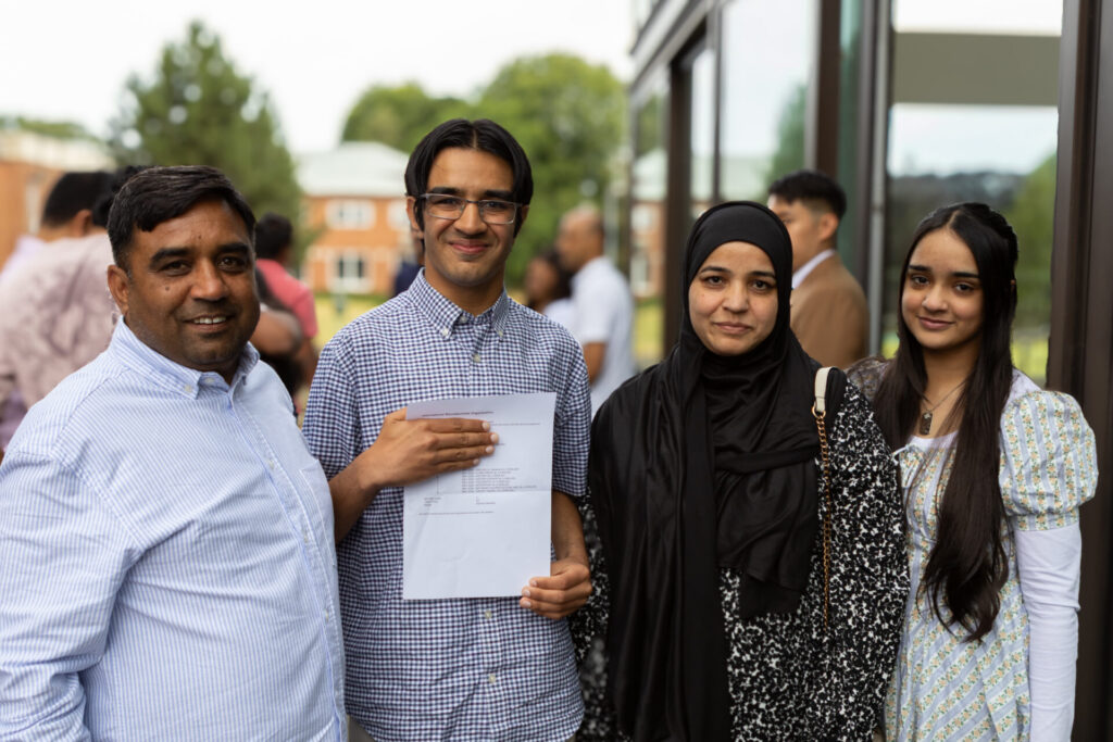 A family poses for a photo while holding a academic results, outside a building.