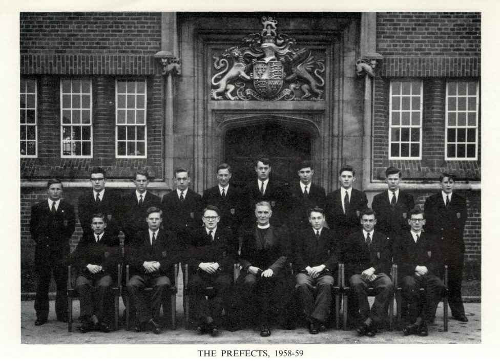 Black and white photograph from 1959, showing the KES prefects. Two rows - one standing and one sitting. Pupils wearing dark coloured blazers, trousers and ties. Chief Master seated centre.