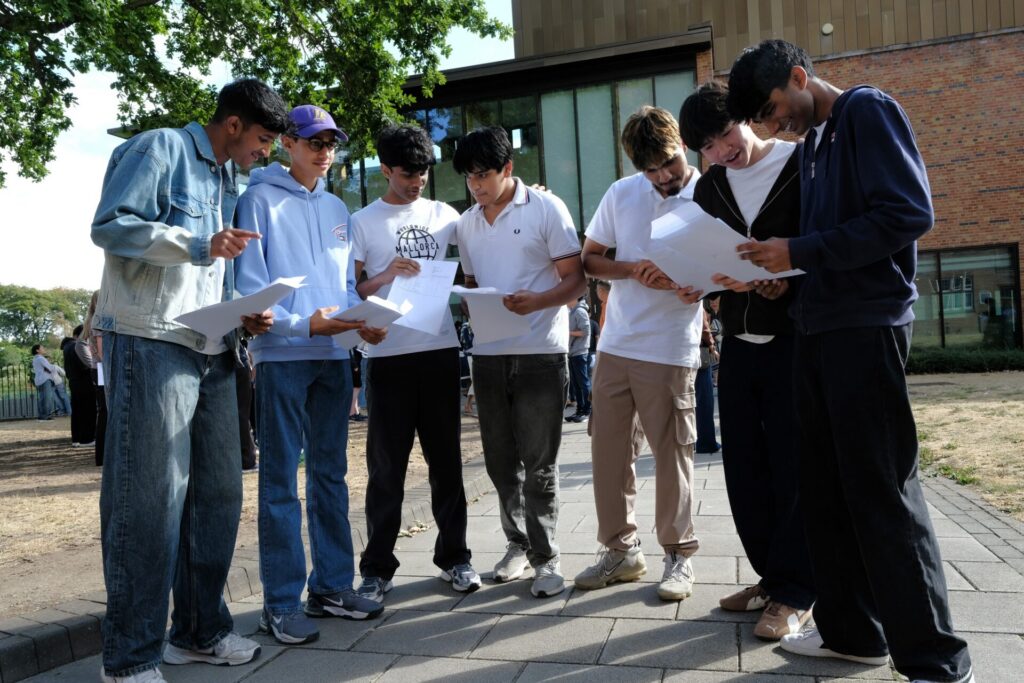 A group of students outdoors smiling and chatting whilst holding exam results.