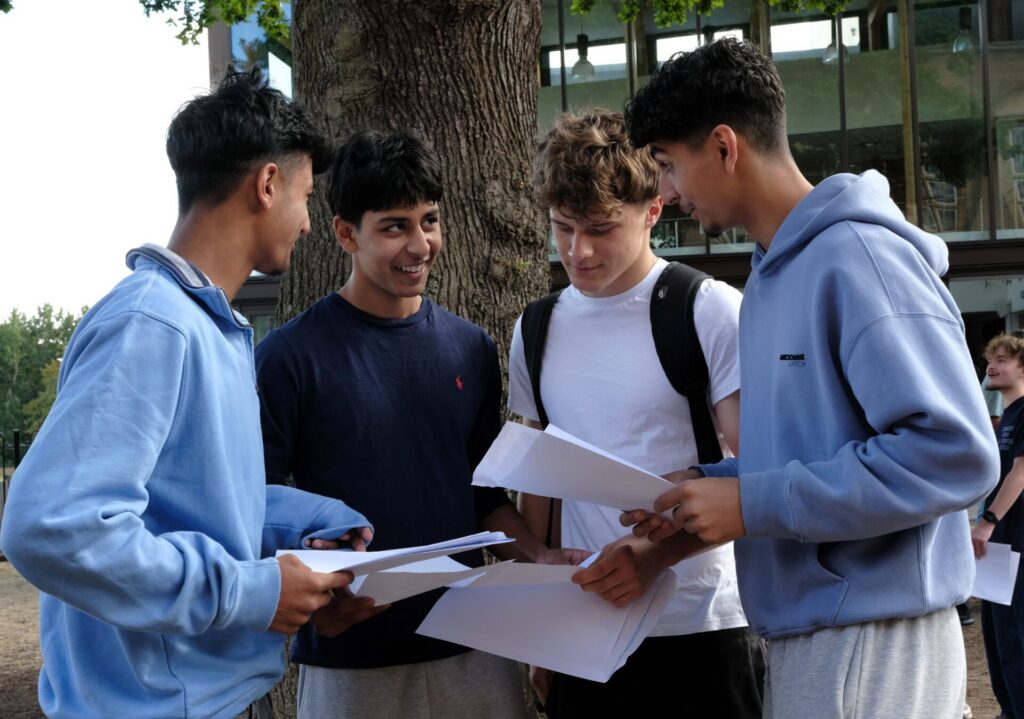 Several students outdoors chatting and smiling holding their exam results.