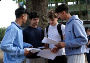 Several students outdoors chatting and smiling holding their exam results.