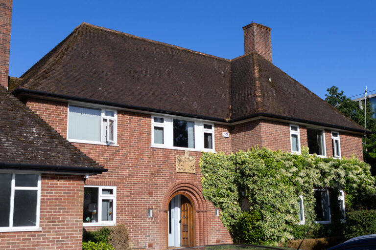 Red-brick house with a wooden door, white-framed windows, and a green ivy-covered wall under a clear blue sky.