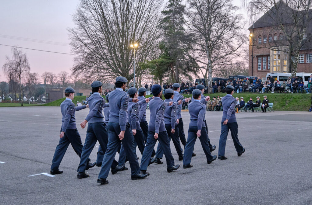 A line of pupils in uniform walking in formation across a paved street.