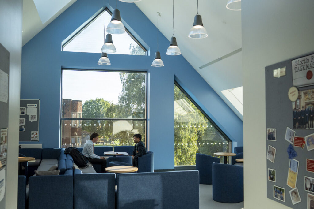 Modern common room with blue walls, and two people seated by a large window overlooking trees.